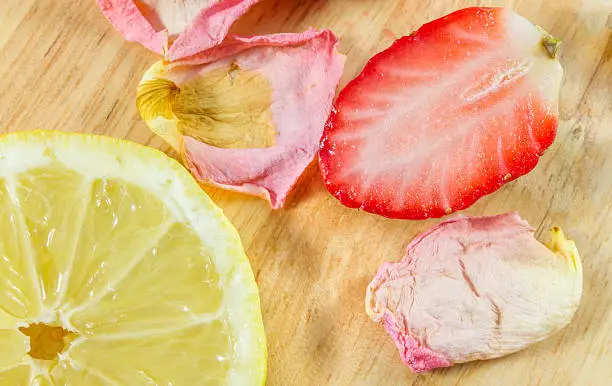 Sliced lemon, strawberry and  rose-petals on wooden board close-up photo