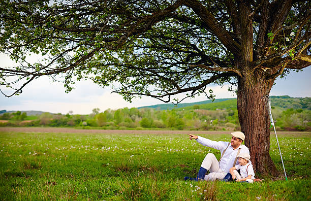 istock farmer father and son sitting under the tree, spring countryside 506604738