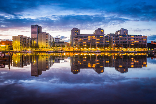 Modern apartment buildings beneath deep blue dusk skies reflecting in the tranquil waters of Kaisaniemenlahti in the heart of Helsinki, Finland's vibrant capital city. ProPhoto RGB profile for maximum color fidelity and gamut.