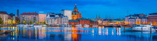 Helsinki harbour Uspenski Cathedral yacht marina illuminated at dusk FInland The iconic domes of Uspenski Cathedral overlooking the redeveloped warehouses, restaurants and waterfront apartments of Katajanokka and the boats moored in the tranquil blue waters of the north habour in the heart of Helsinki, Finland's vibrant capital city. ProPhoto RGB profile for maximum color fidelity and gamut. famous landmarks in finland stock pictures, royalty-free photos & images
