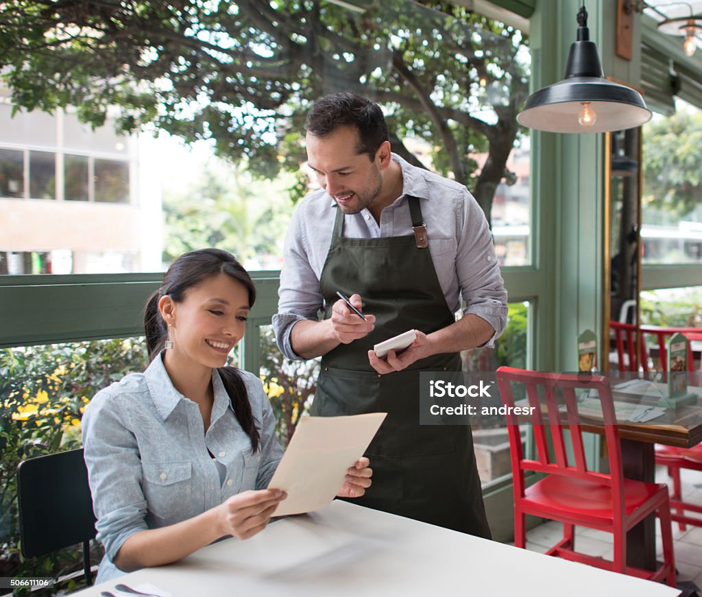 Woman eating at a restaurant Woman eating at a restaurant and looking at the menu while the waiter makes suggestions and waits to take the order Customer Stock Photo