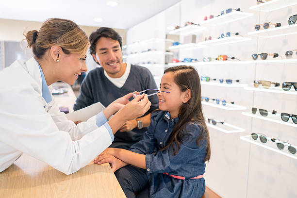 Girl at the optician's shop trying new glasses Happy girl at the optician's shop with her father and the eye doctor and trying new glasses optical equipment stock pictures, royalty-free photos & images