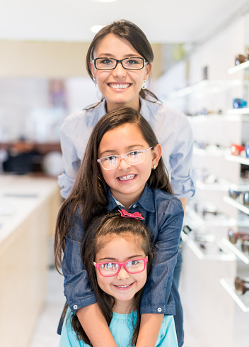 Happy Mother and daughters wearing glasses at the opticianâs shop and looking at the camera smiling