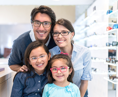 Happy Latin American family wearing glasses at the opticians shop and looking at the camera smiling