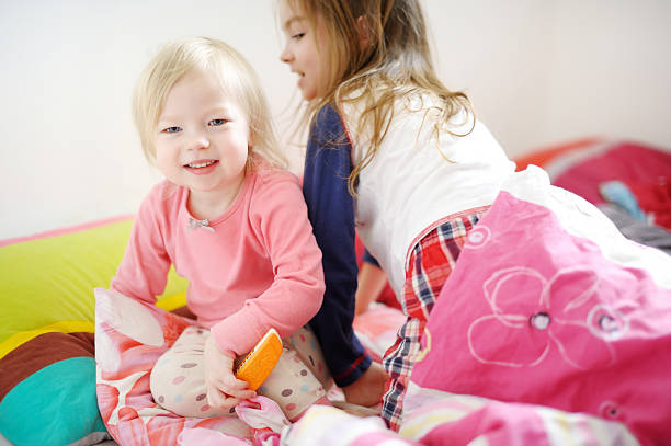 Two little sisters playing in bed on sunny morning