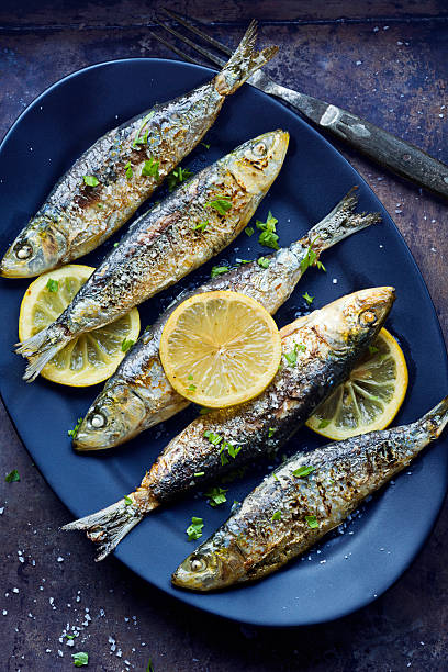 Grilled Portuguese Sardines with Salt, Herbs and Lemon Portuguese sardines are rolled in salt and grilled over an open flame. These are served with parsley and grilled lemon slices. This photo works well as both a vertical and a horizontal image. sardine photos stock pictures, royalty-free photos & images