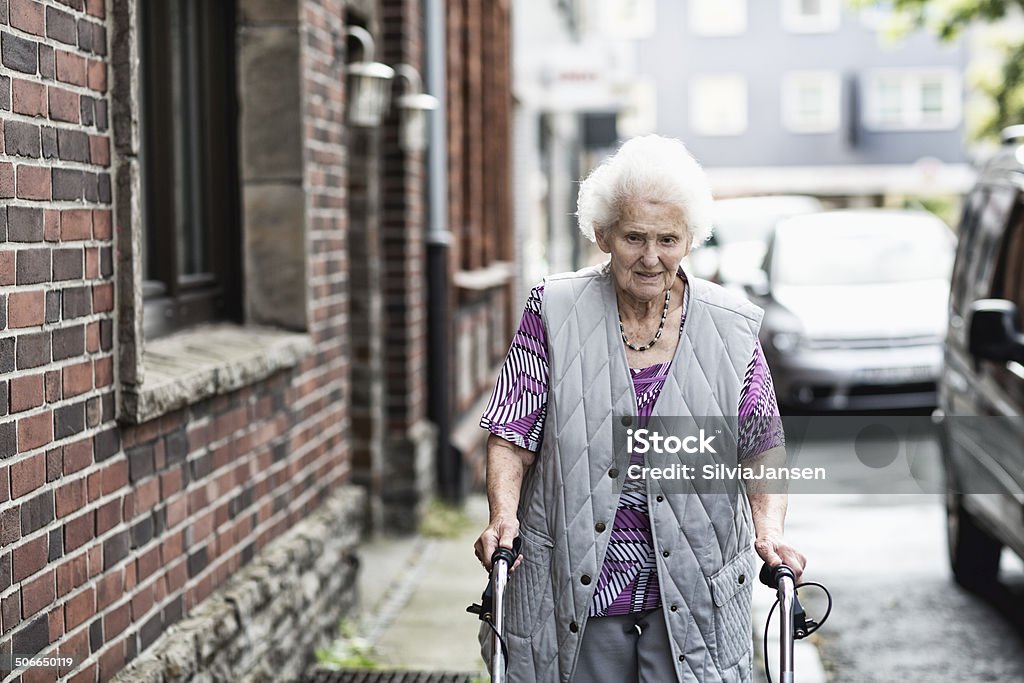 senior woman lonely senior woman walking, supported by a walker, in a run down district Poverty Stock Photo