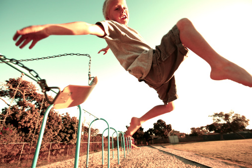 This is a photo of a young boy jumping off a swing on a sunny blue sky day.