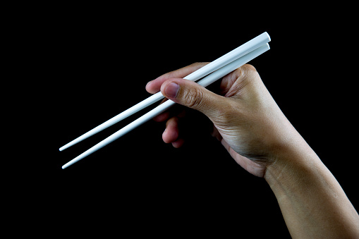 Hand holding white chopsticks isolated against a black background