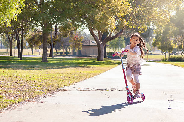 Little girl riding her scooter in the park stock photo