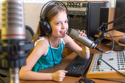 Cute little girl  radio DJ sitting before microphone in studio