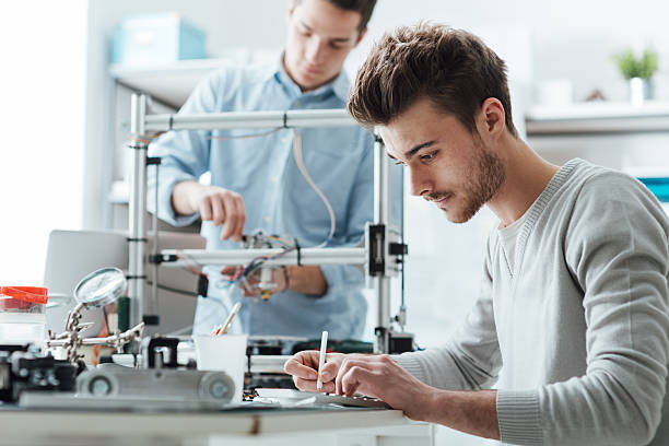 Engineering students working in the lab Engineering students working in the lab, a student is using a 3D printer in the background 3d printing lab stock pictures, royalty-free photos & images