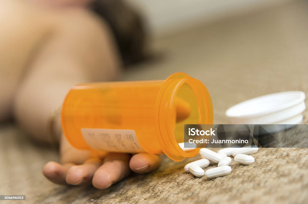 A hand at the floor holding a box with drugs woman lying on the floor unconscious  after taking prescription drugs Addiction Stock Photo