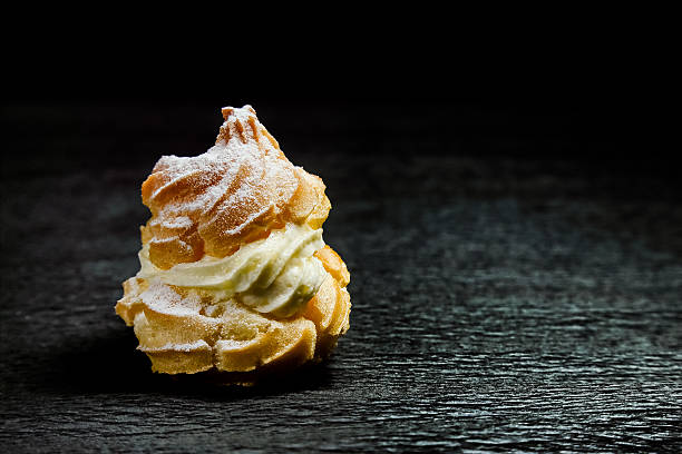 Close up of a cream puff on a rough dark surface. Isolated on black.