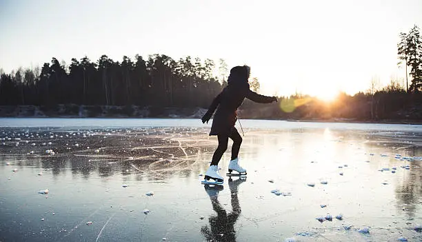 Ice skating on the frozen lake. Young woman on ice skates in sunset.
