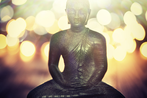 Buddha statue on blurred lights background. Shallow DOF - focus on the face