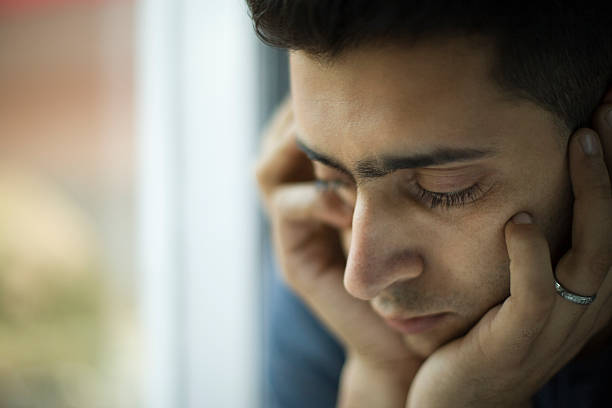 Young jobless man holding his head and thinking near window. stock photo