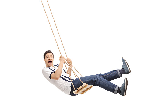 Delighted young guy swinging on a wooden swing and looking at the camera isolated on white background