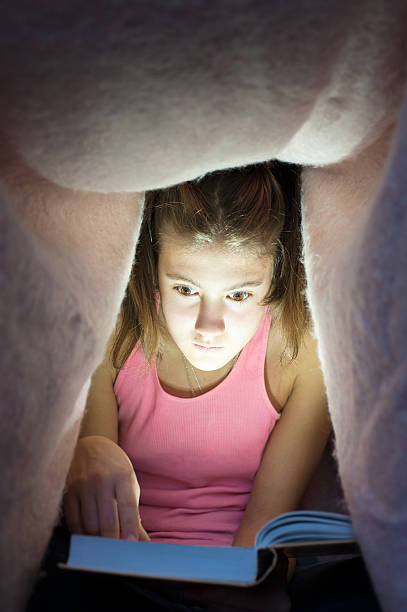 istock Young girl hiding under blanket and enrapt reading interesting book 506714588