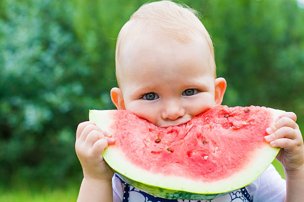 niedliche kleine mädchen essen wassermelone auf dem rasen im sommer - watermelon fruit summer portion stock-fotos und bilder