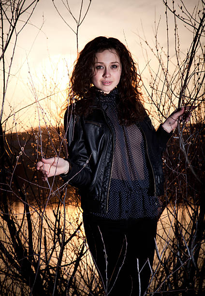 istock Curly woman in blouse standing on beach against sunset light 506731679
