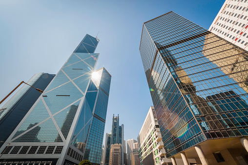 Bright sunlight bursting through the glass canyons of skyscrapers and dowtown business towers as they reach for clear blue skies, Hong Kong, China. ProPhoto RGB profile for maximum color fidelity and gamut.