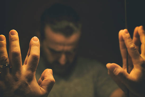 Man in despair with raised hands and bowed headd, in a low light room looking in front of mirror