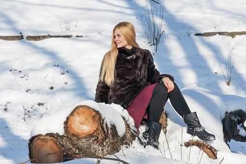 Beautiful woman sitting on the log. Winter portrait