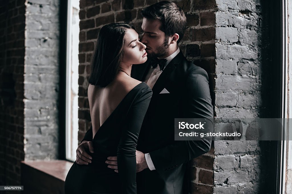 Beauty and passion. Beautiful young loving couple bonding to each other while both standing against brick wall indoors Sensuality Stock Photo