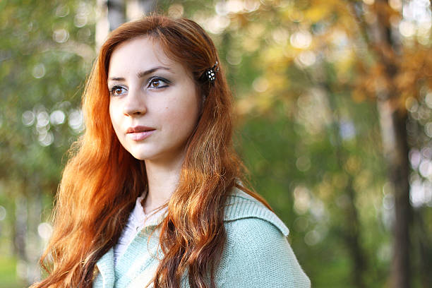 Ginger girl with expressive face posing outdoor. Red haired woman with nordic appearance walks in park.