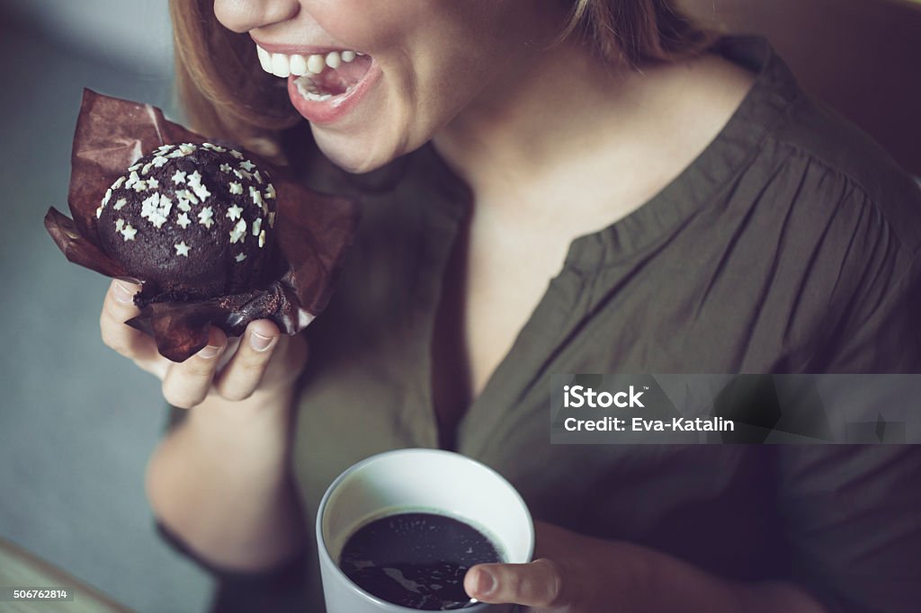 Having breakfast Young woman is eating chocolate muffin Eating Stock Photo