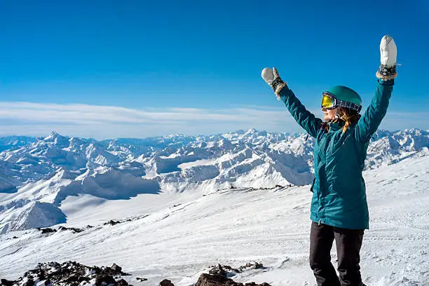 Happy young woman with arms raised on background of the snowy high mountains and beautiful landscape