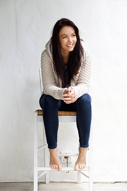 lunghezza completa di sorridente giovane donna seduta su una sedia - 30s women sweater female foto e immagini stock