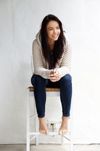 Full length portrait of a smiling young woman sitting on chair