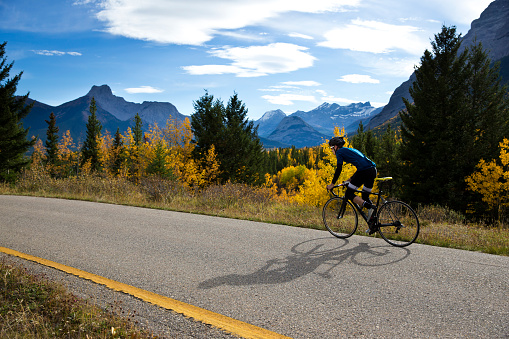 A male road cyclist rides a quiet country lane in the Rocky Mountains of Canada in the fall.