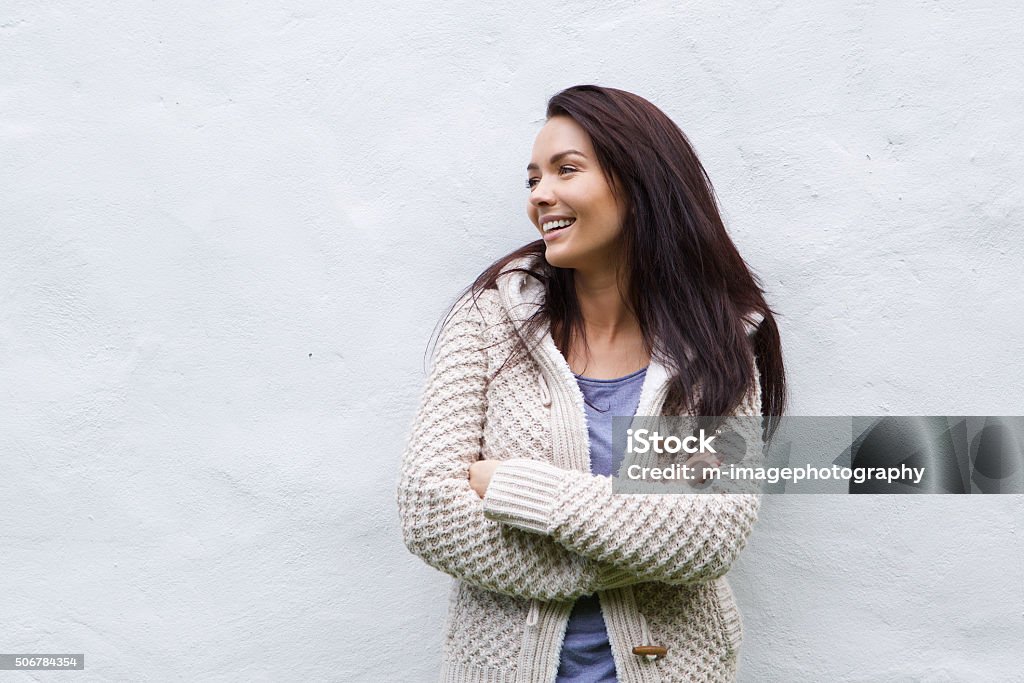 Mulher sorridente em malha de lã branca em pé contra a parede - Foto de stock de Mulheres royalty-free