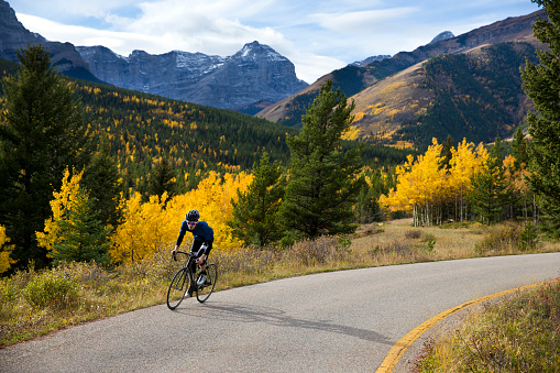 A male road cyclist rides a quiet country lane in the Rocky Mountains of Canada in the fall.
