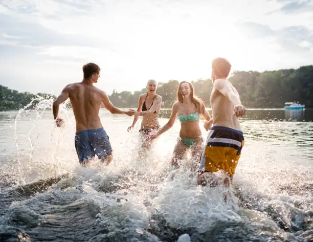 Two young couples having fun and running into a lake.