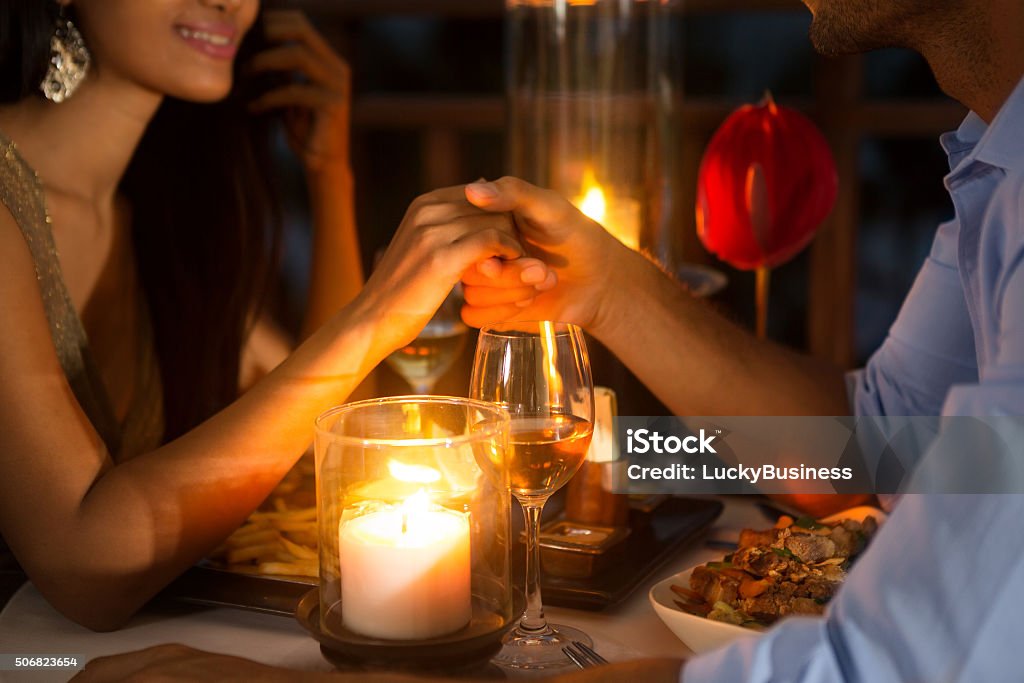 Romantic couple holding hands together over candlelight Romantic couple holding hands together over candlelight during romantic dinner Dinner Stock Photo