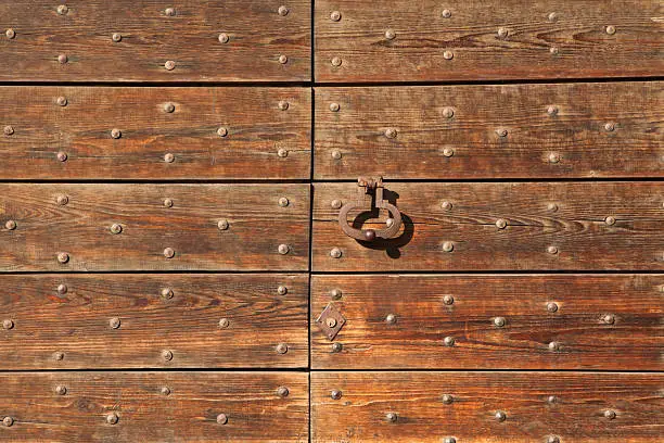 Old metal doorknocker on the wooden gate fixed with rivets in Bergamo, Lombardy, Italy.