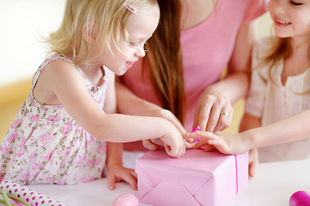 Mother and het two daughters wrapping a gift Young mother and her two little daughters wrapping a gift with pink wrapping paper birthday wishes for daughter stock pictures, royalty-free photos & images
