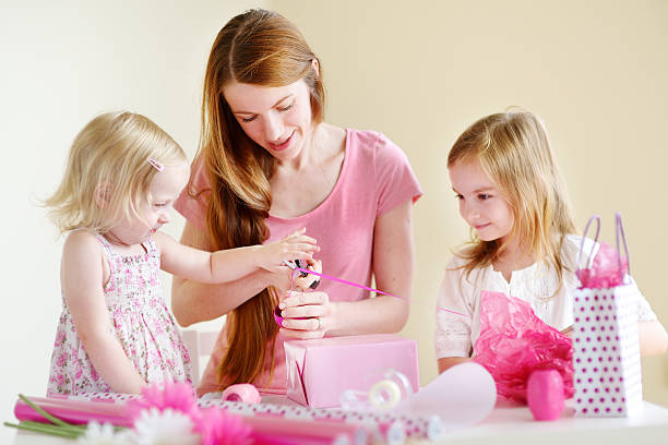 Mother and het two daughters wrapping a gift Young mother and her two little daughters wrapping a gift with pink wrapping paper birthday wishes for daughter stock pictures, royalty-free photos & images