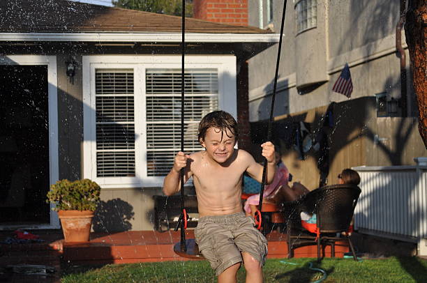 Boy swinging through a sprinkler stock photo