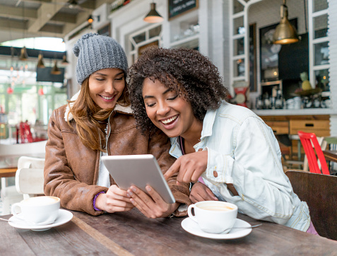 Happy women at a cafe having a cup of coffee and social networking using a tablet computer