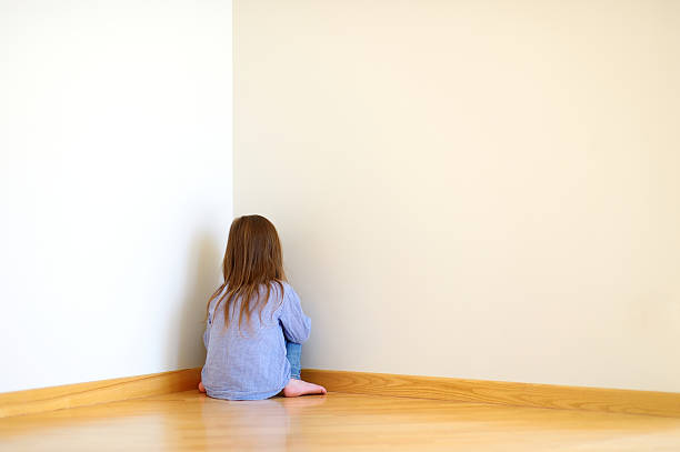 Sad little girl sitting in a corner stock photo