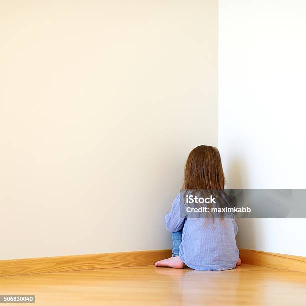 Sad Little Girl Sitting In A Corner Stock Photo - Download Image Now - Behind, Child, Sadness