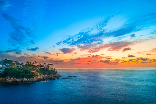 Photo of colorful expansive sky with clouds, coastline and the Pacific Ocean in Acapulco, Mexico at sunset.