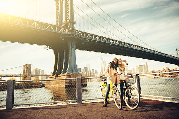 Two girl friends riding their bicycles along The East River in New York City.