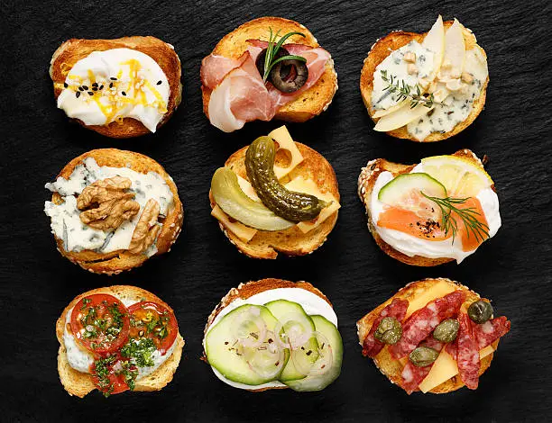 Delicious appetizers with slices of  baguette and various toppings on stone black background