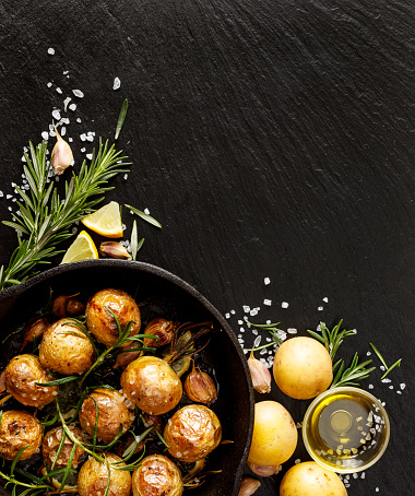 Roasted potatoes with rosemary, garlic, lemon and sea salt on a black background. Vegetarian dish nutritious and delicious